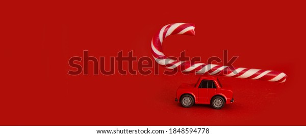 Christmas banner mockup. Concept of a car for\
delivering Christmas gifts. A red car carries a candy cane on a red\
background. Front view creative abstract banner composition with\
place for text.