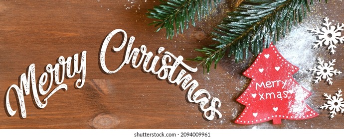 Christmas banner with text 'Merry Christmas', snowy fir tree branch and decorations on wooden background