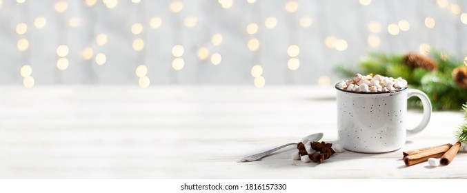 Christmas banner with white cup with hot chocolate and marshmallows on with cinnamon sticks and fir xmas tree branches with beautiful garland lights. New year celebration