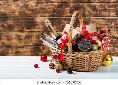 Christmas basket with champagne bottle and glasses, gifts with red satin ribbon, candy canes, pine cones, golden garlands on dark brown wooden background - Powered by Shutterstock