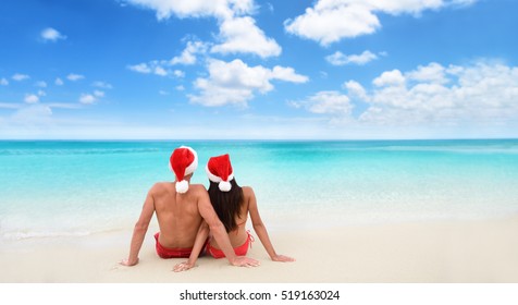 Christmas beach vacation holidays santa hat couple relaxing from behind sitting on white sand wide horizontal sky background for text advert for holiday season. Blue ocean texture. - Powered by Shutterstock