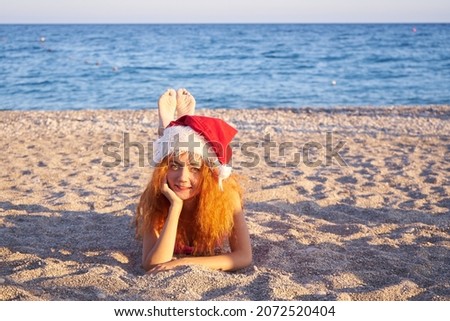 Christmas beach vacation travel woman wearing Santa hat and pink bikini enjoying winter holidays on tropical beach.Woman in Santa hat sitting on the beach luxury resort.