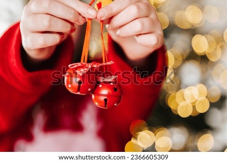 Christmas Bells .child holding red and white decorative bells in his hand on a shining Christmas tree background. Christmas tree decoration with bells.Holiday accessories