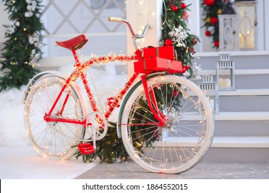 A Christmas bike with garlands stands on a large white New Year's veranda decorated with Christmas trees and red and gold balls