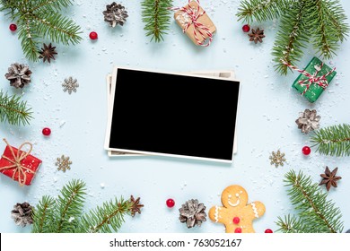 Christmas Blank Photo Card In Frame Made Of Fir Tree Branches, Decorations And Gift Boxes Over Blue Background. Mock Up. Flat Lay. Top View