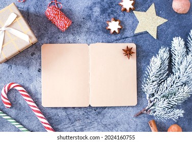 Christmas Book Background Frame Mockup From Notepad With White Sheets Of Copy Space On A Blue Background Near Lollipops Cane, Fir Branch, Star Cookies, Flat Lay