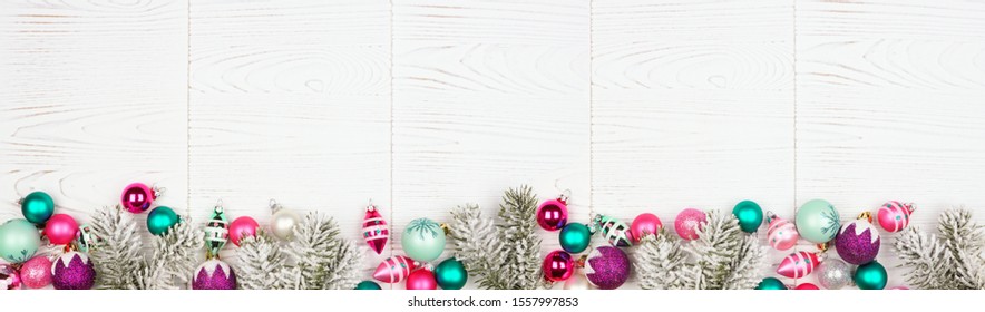 Christmas Border Banner With Pink, Purple And Teal Decorations And Tree Branches. Overhead View On A White Wood Background.