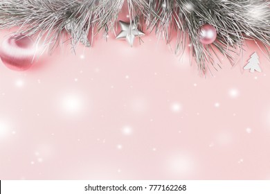 Christmas border with fir branches, christmas balls and silver ornaments on pastel pink background, snow falling