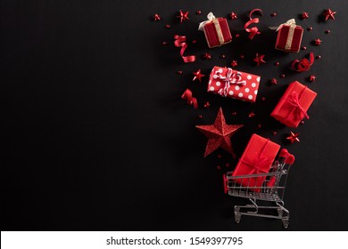 Christmas and Boxing Day background concept. Top view of shopping cart splash out Christmas decoration with gift box red star berries and ribbon on black background. - Powered by Shutterstock