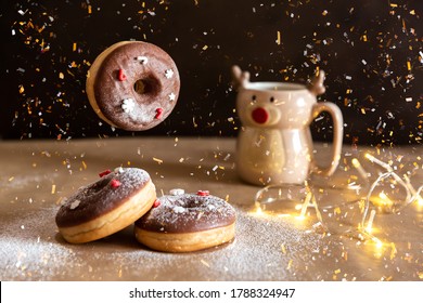 Christmas Breakfast Table With Flying Chocolate Donut Decorated With Red And White Sprinkles, Hot Cocoa In Deer Mug On Background