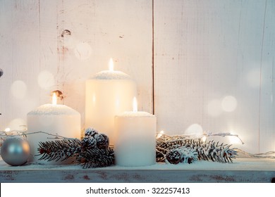 Christmas Candles And Snowy Fir Branches Over White Wooden Background With Lights