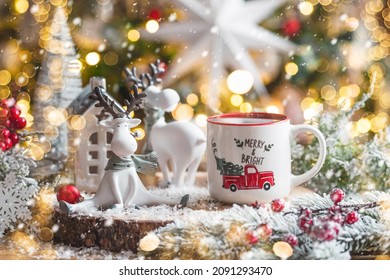 A Christmas card with cute reindeer and a mug of hot coffee on the background of a beautiful bokeh. New Year's still life. The concept of a home holiday, warmth and comfort.