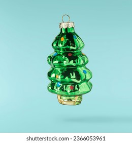 Christmas card. Falling in the air Christmas bauble in the shape of christmas tree isolated on blue background. Christmas figurine. Levitation or zero gravity conception. High resolution image.