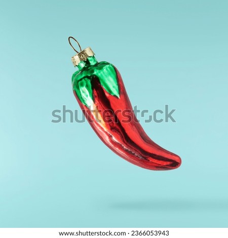 Christmas card. Falling in the air Christmas bauble in the shape of red chili pepper isolated on blue background. Christmas figurine. Levitation or zero gravity conception. High resolution image.