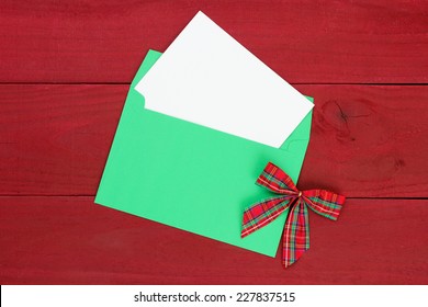 Christmas Card And Green Envelope With Red Plaid Bow On Antique Red Wooden Background