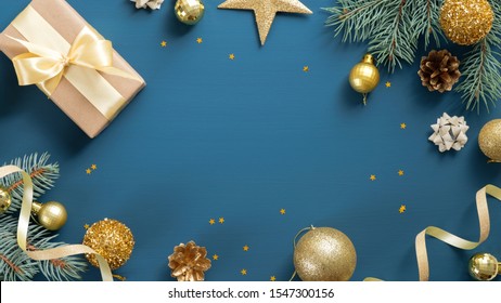 Christmas card with pine tree branches, gifts, golden decorations over blue background. Flat lay, top view, copy space. Christmas frame, New year banner mockup