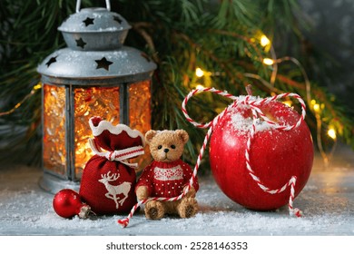 Christmas card with teddy bear, red apple and gift bag on table, lantern, spruce and pine branches with light garland - Powered by Shutterstock