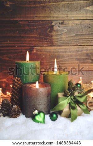 Christmas card - Third Advent. Green burning  christmas candles with gift box in snow on rustic wooden background