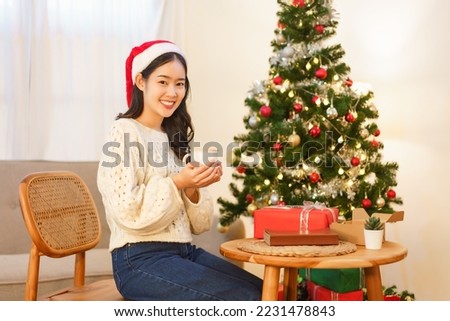 Christmas celebration concept, Asian woman sits on chair near christmas tree and holding coffee cup.