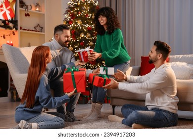 Christmas celebration. Happy friends exchanging gifts at home - Powered by Shutterstock