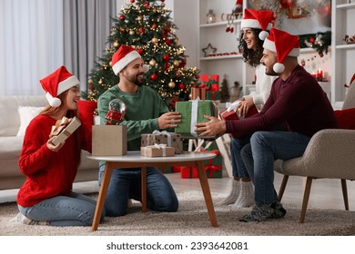 Christmas celebration. Happy friends in Santa hats exchanging gifts at home - Powered by Shutterstock