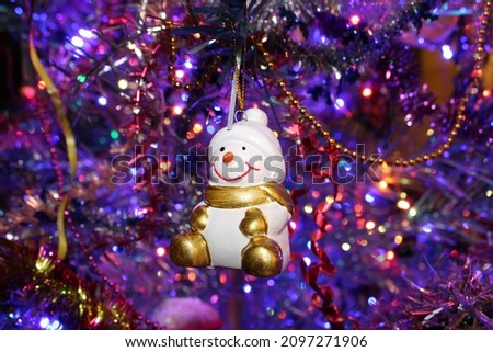 Christmas ceramic snowman with golden scarf, mittens and felt boots on the background of blue and red shining garlands. Creates a real festive atmosphere of Christmas and New Year.