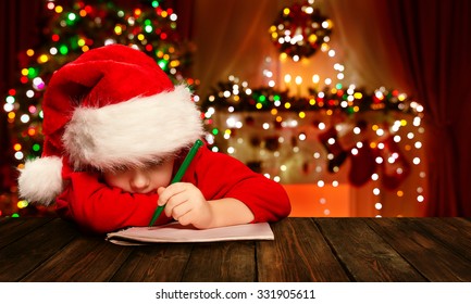 Christmas Child Write Letter To Santa Claus, Kid In Santa Hat Writing Wish List, Unfocused Lights Background