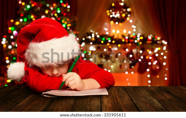 ぼかした光の背景にクリスマスの子どもがサンタクロースに手紙を書く サンタハットの子どもがウィッシュリストを書く の写真素材 今すぐ編集