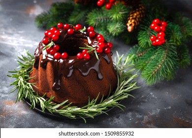 Christmas chocolate bundt cake with glaze decorated with fresh berries and rosemary. Winter baking at Xmas or New Year with decorations on dark background