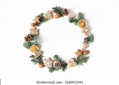 Christmas circle floral composition. Wreath of fir tree branches, pine cones, gingerbread cookies and dry orange slices on white background. Winter holiday design, flat lay, top view. - Powered by Shutterstock