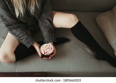 Christmas, cold autumn or winter day. Warming mood. Woman drinking warm cocoa with marshmallows. Lazy weekend in knitted sweater on the couch. Cozy scene, hygge concept