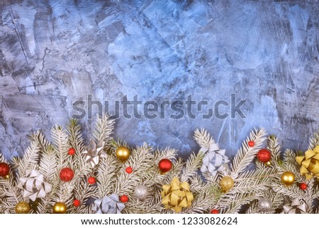 Christmas composition with copy space. On a blue background with the texture of plaster laid out covering the frost branches of spruce. Red and gold balls and bows adorn the composition of fir