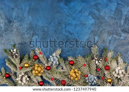 Christmas composition with copy space, on a dark blue background with stucco texture. Spruce branches are covered with hoarfrost and decorated with Christmas balls and bows. Festive layout with place