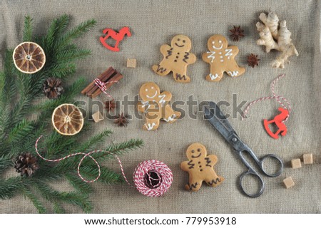 Christmas composition with gingerbread in the form of little men and spruce branches. The composition is supplemented with a root of ginger, braid, spices, scissors. Canvas background. View from above