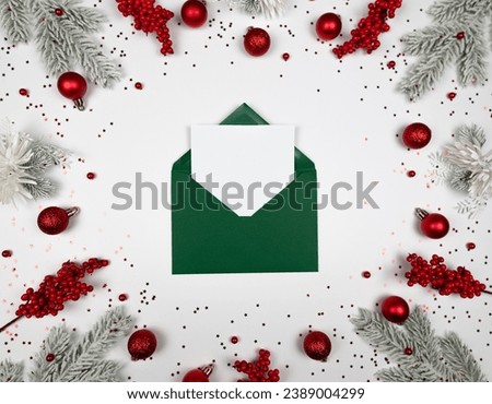 Christmas composition, green envelope, fir tree branches, red berries, baubles and stars confetti on white background. Christmas, New Year, winter concept. Top view, flat lay, copy space. 