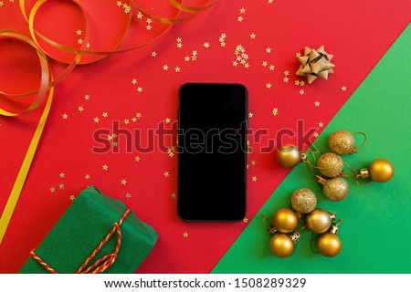 Christmas composition. Green gift box, mobile phone on red and green background with golden confetti. new year concept. Greeting card, xmas celebration 2020. Flat lay, top view, copy space, mockup