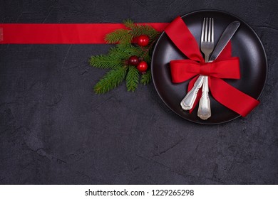 Christmas composition with plate, cutlery, pine branches, ribbon and red berries on black table. Winter holidays and festive background. Christmas eve dinner, New Year food lunch.  top view - Powered by Shutterstock