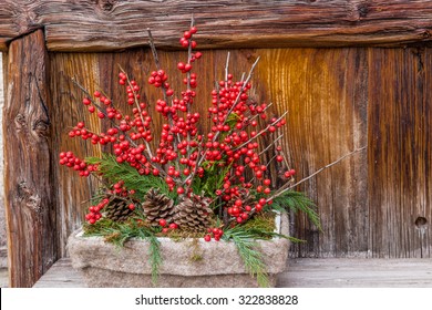 Christmas composition with red berries of mistletoe, brown  pine cones and green branches in a rectangular  vase on an old wooden fence