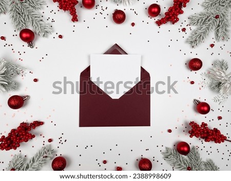 Christmas composition, red envelope, fir tree branches, red berries, baubles and stars confetti on white background. Christmas, New Year, winter concept. Top view, flat lay, copy space. 