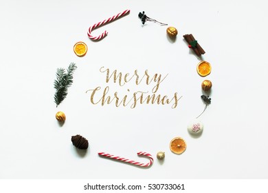 Christmas composition. christmas round frame, candy cane orange cinnamon sticks gingerbread tree walnuts top view merry christmas text on white background flat lay copy space 