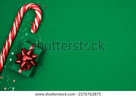 Christmas composition. Striped candy cane and gift box on green background. Flat lay, top view, copy space.