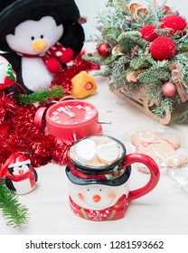 Christmas composition at the table with the decor, a mug of marshmallows in the form of a snowman, a penguin and a red clock