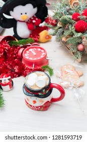 Christmas composition at the table with the decor, a mug of marshmallows in the form of a snowman, a penguin and a red clock