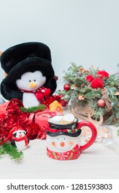 Christmas composition at the table with the decor, a mug of marshmallows in the form of a snowman, a penguin and a red clock