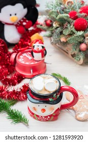Christmas composition at the table with the decor, a mug of marshmallows in the form of a snowman, a penguin and a red clock