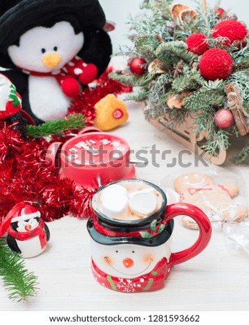 Christmas composition at the table with the decor, a mug of marshmallows in the form of a snowman, a penguin and a red clock