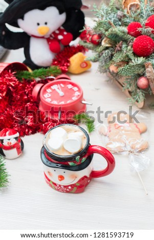 Christmas composition at the table with the decor, a mug of marshmallows in the form of a snowman, a penguin and a red clock