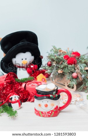 Christmas composition at the table with the decor, a mug of marshmallows in the form of a snowman, a penguin and a red clock