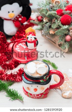 Christmas composition at the table with the decor, a mug of marshmallows in the form of a snowman, a penguin and a red clock