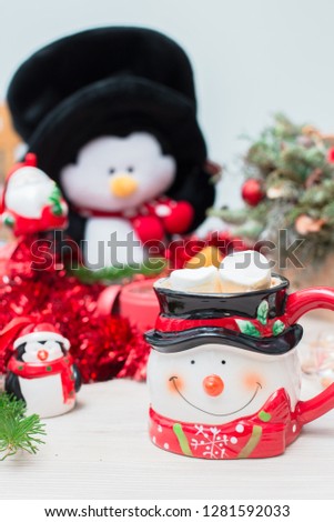 Christmas composition at the table with a decor, a snowman mug, a penguin and a red clock